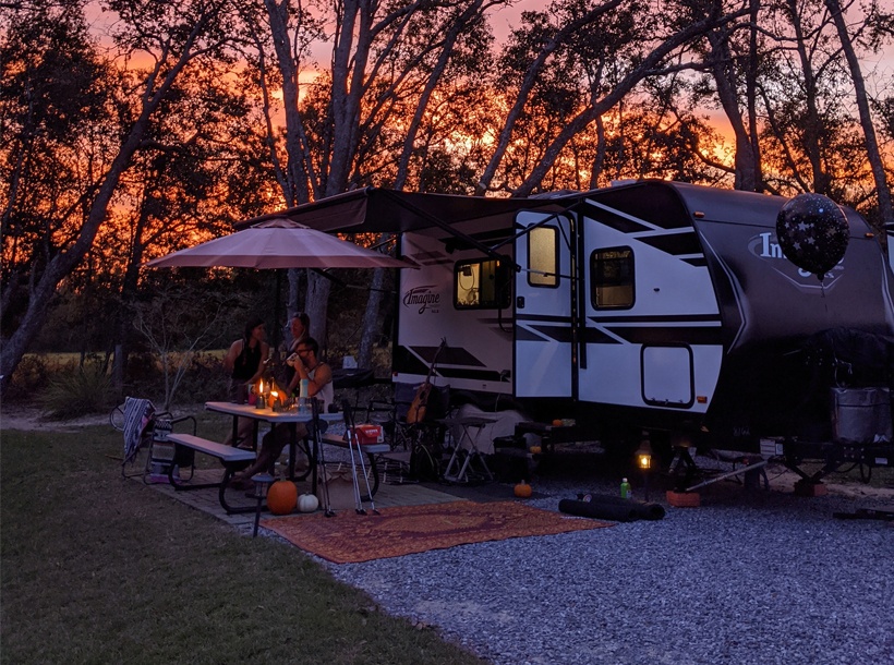 An RV parked in a secluded wooded site at sunset
